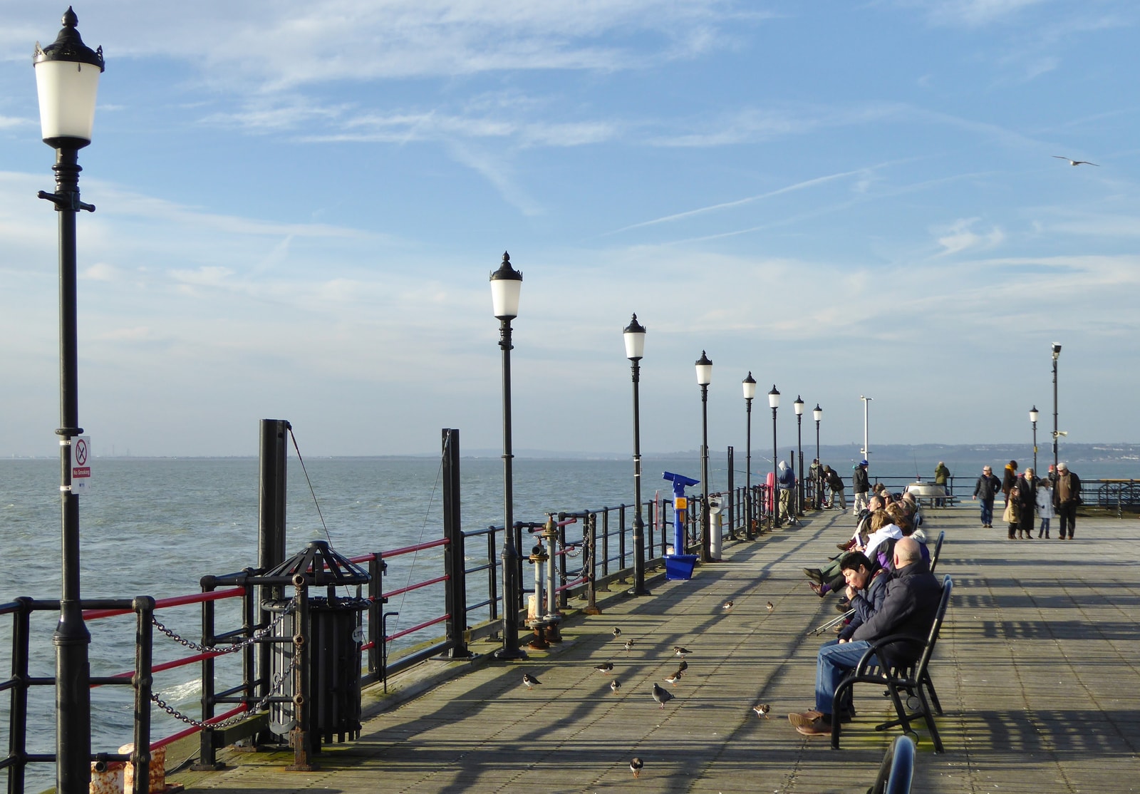 People relaxing in the sun on the wooden boardwalk of Southend Pier.
