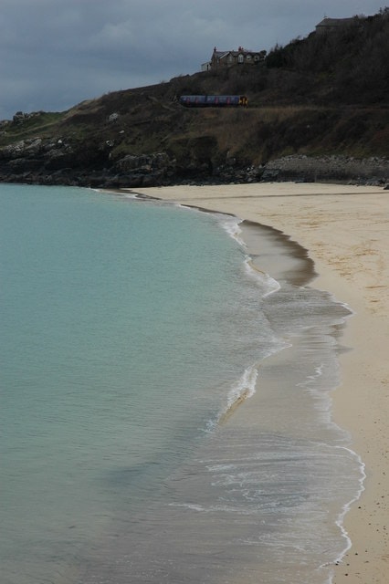 A train on the St Ives Bay Line travels along the tracks situated just above the golden sands and blue waters of Porthminster Beach.