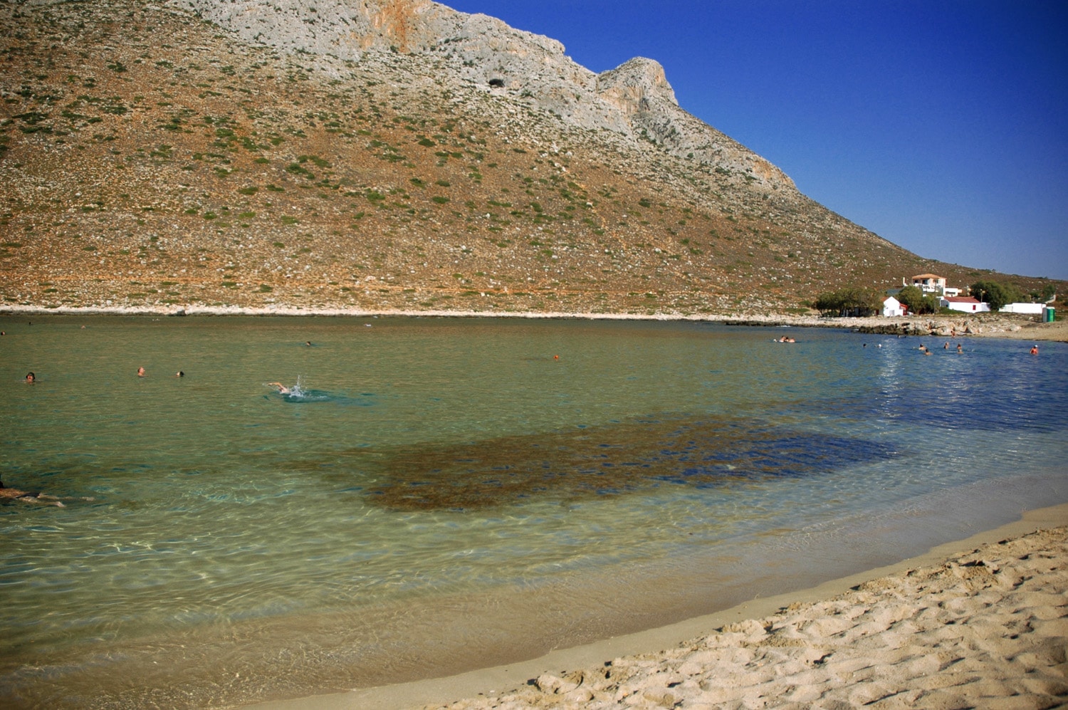 The calm, lagoon-like bay of Stavros Beach is nestled against the iconic camel-shaped Vardies Mountain.