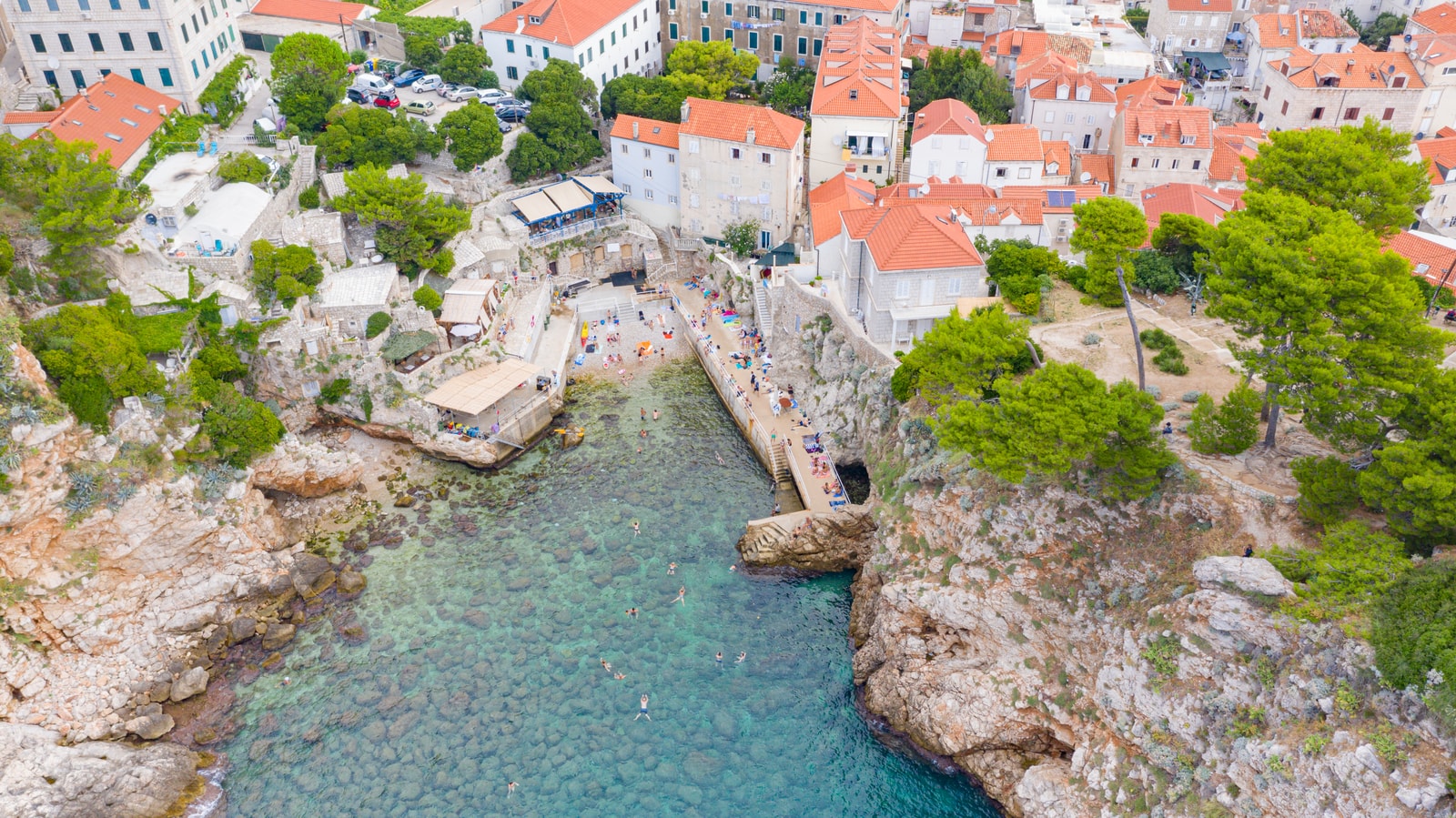 An aerial shot captures the intimate, emerald-water cove of Šulić Beach, located near Dubrovnik's historic center.