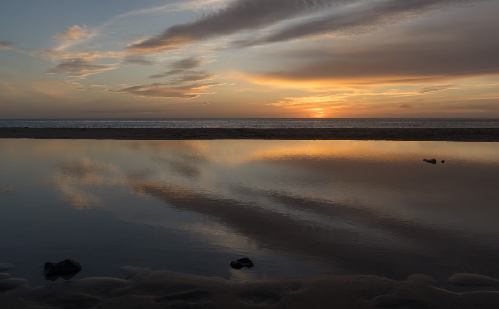 A stunning sunset over Playa del Castillo, with golden clouds reflected in a tidal pool on the sand.