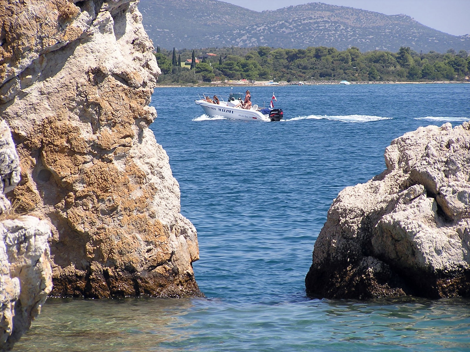 A view of the pine-covered Sustipanac Islet, also known as the Island of Love, seen from the rocky shore.