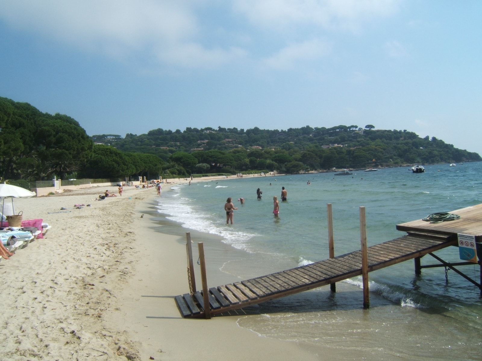 A wooden ramp slopes down to the calm, shallow azure waters at Tahiti Beach, with pine forests in the background.