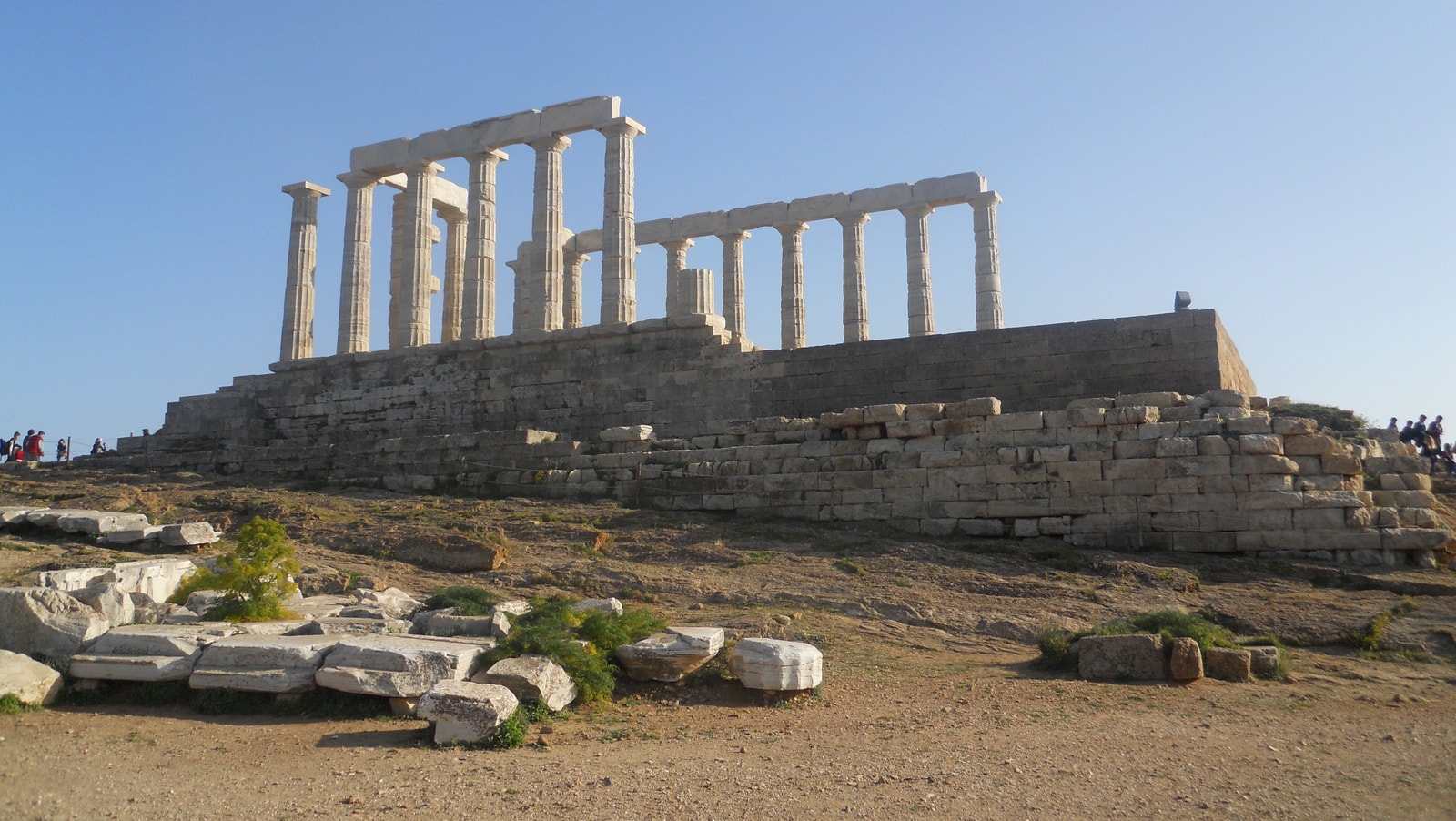 The ancient columns of the Temple of Poseidon stand on a cliff overlooking the blue sea.