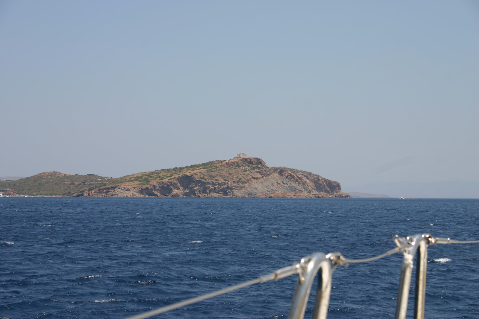 A photo of the Temple of Poseidon taken from a boat on the sea, showing its prominent position on the cliff.