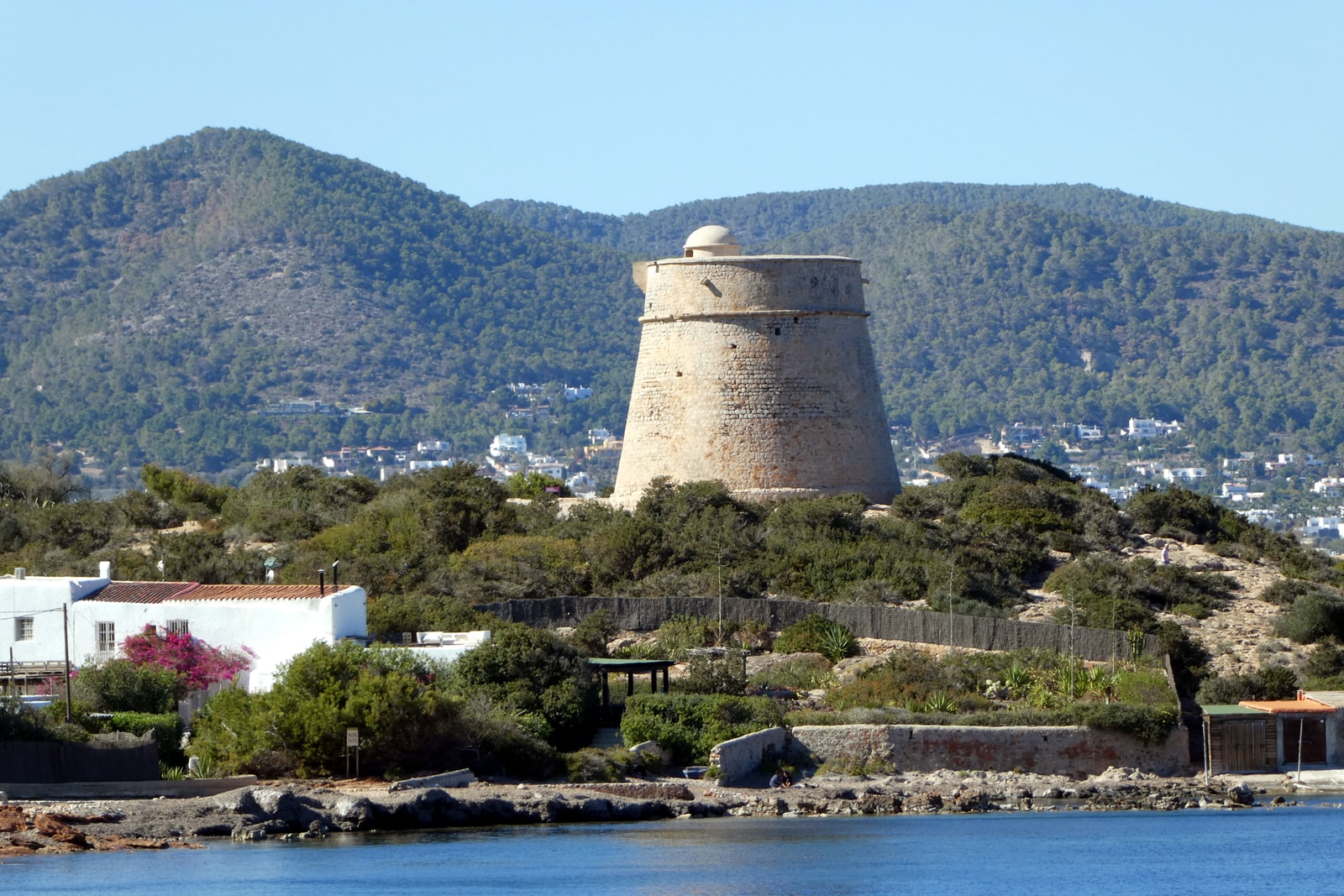 The historic 16th-century stone watchtower, Torre de sa Sal Rossa, with vibrant bougainvillea flowers in the foreground.