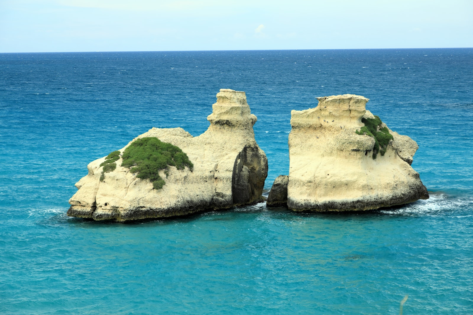 Two majestic limestone sea stacks, known as Le Due Sorelle (The Two Sisters), rising from the turquoise sea at Torre dell'Orso.