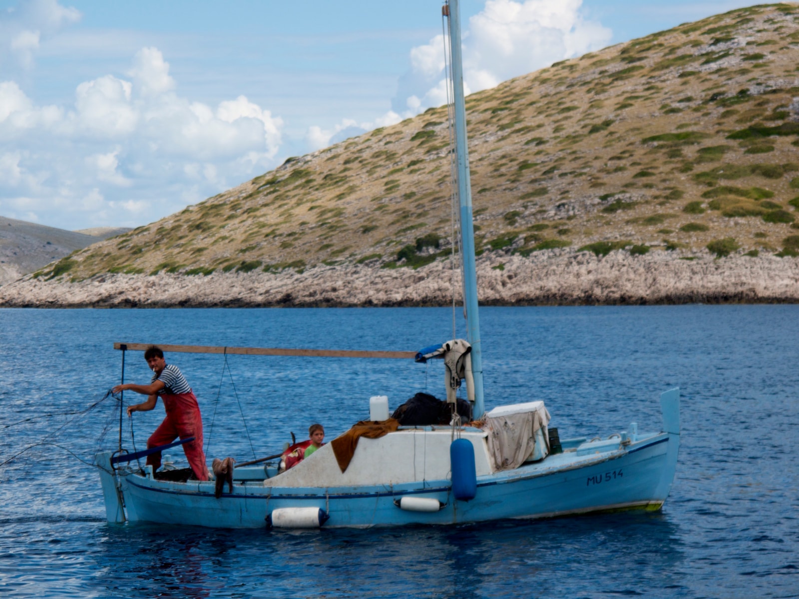 A traditional fisherman casts his net from a wooden boat in the clear waters of the Kornati archipelago.