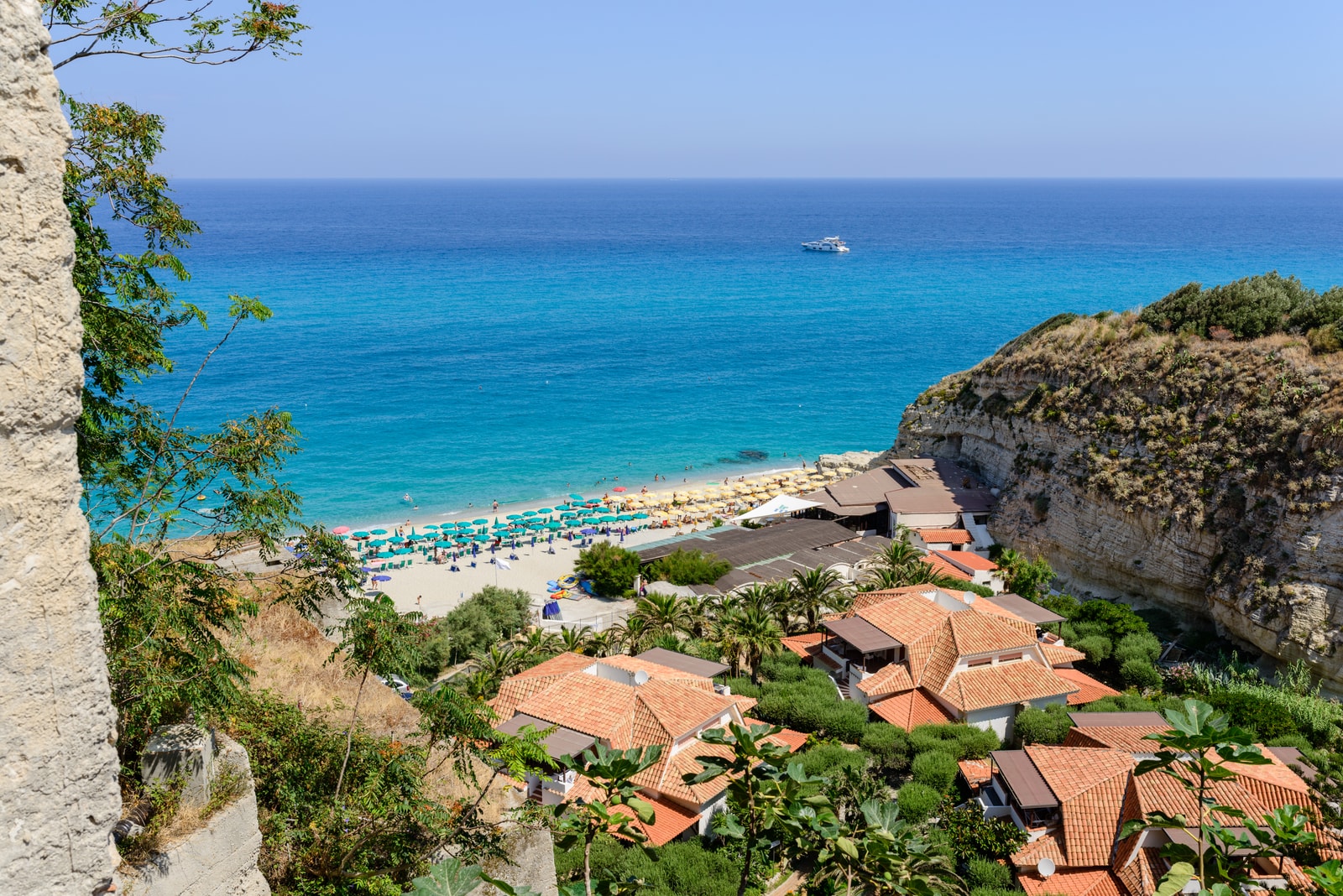 Terracotta roofs of Tropea's clifftop buildings overlook the golden sand and blue umbrellas of the beach below.