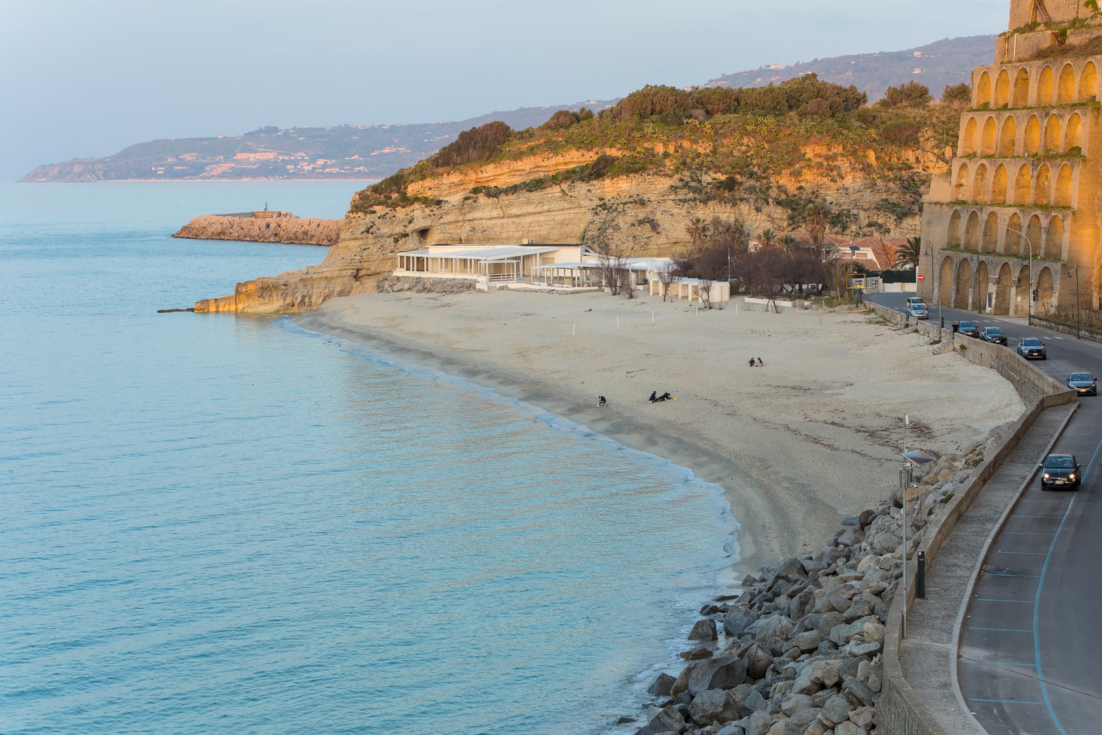 A beachside restaurant and cove are bathed in the warm golden light of a sunset in Tropea.