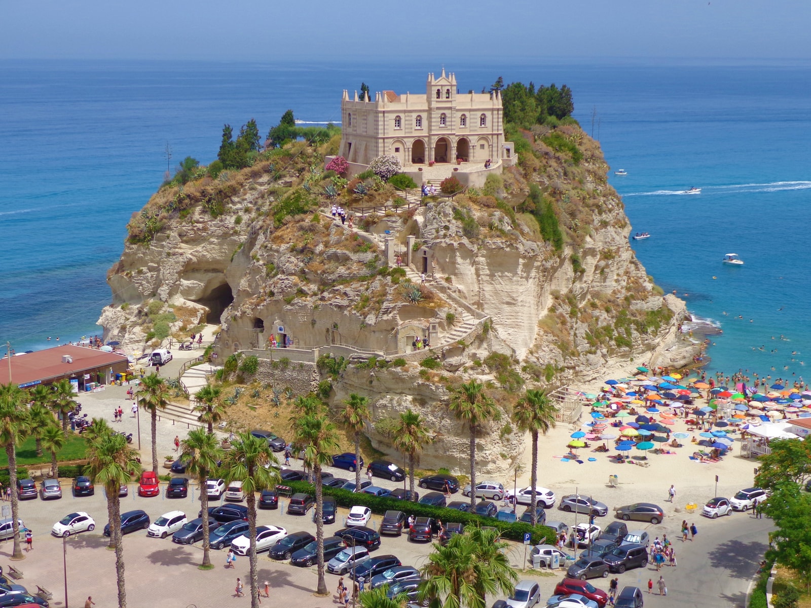 Stone staircases and pathways shaded by palm trees lead down towards the beach from the Sanctuary of Santa Maria dell'Isola.