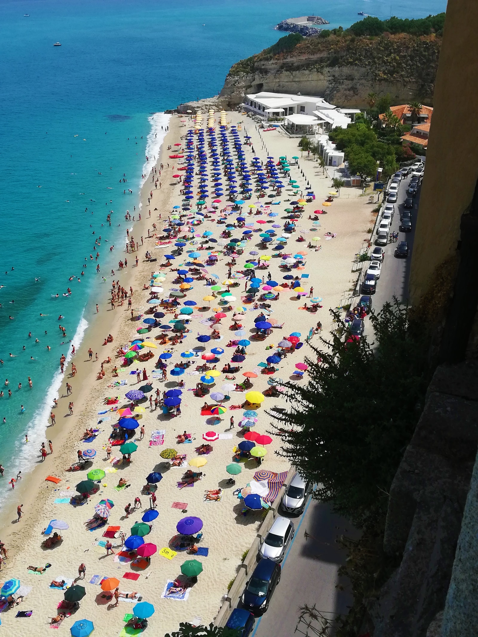 A bird's-eye view of neat rows of matching blue umbrellas and sunbeds at a lido on Spiaggia della Rotonda.