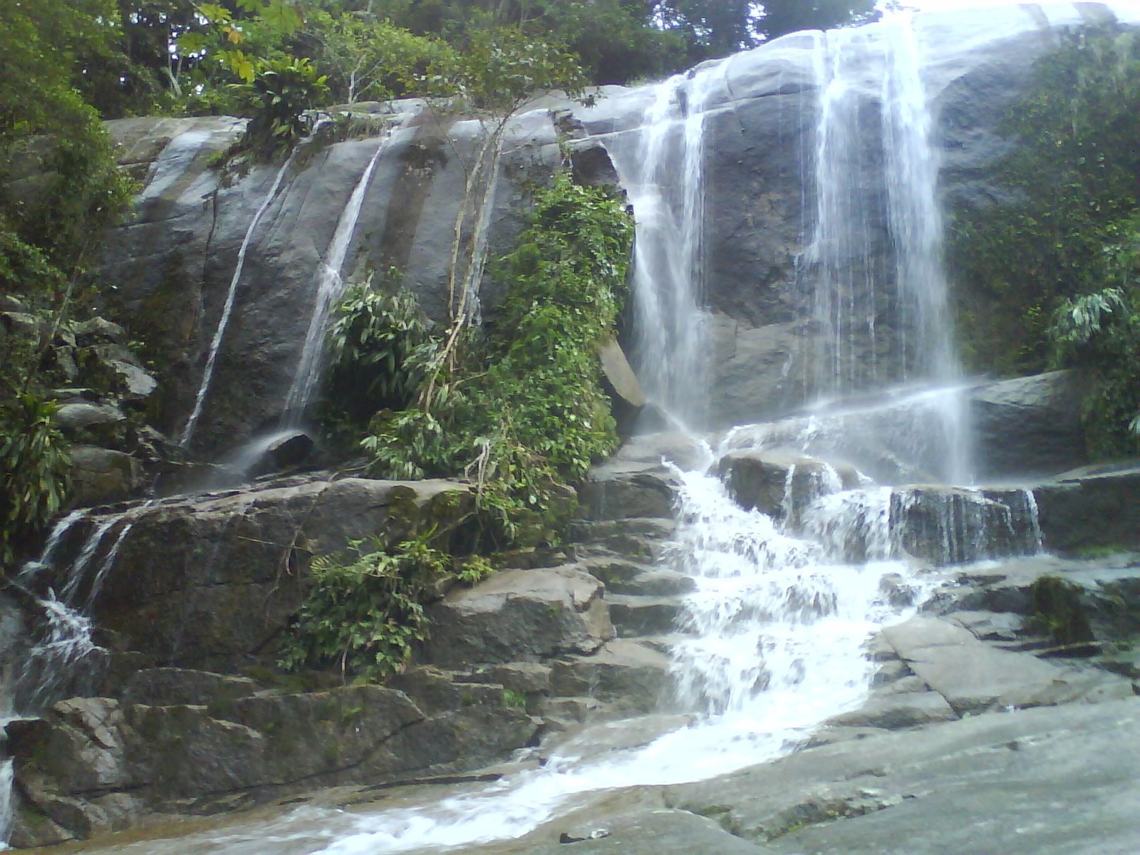 A waterfall named Cachoeira da Escada cascades over rocks next to the Rio-Santos highway, surrounded by lush greenery.