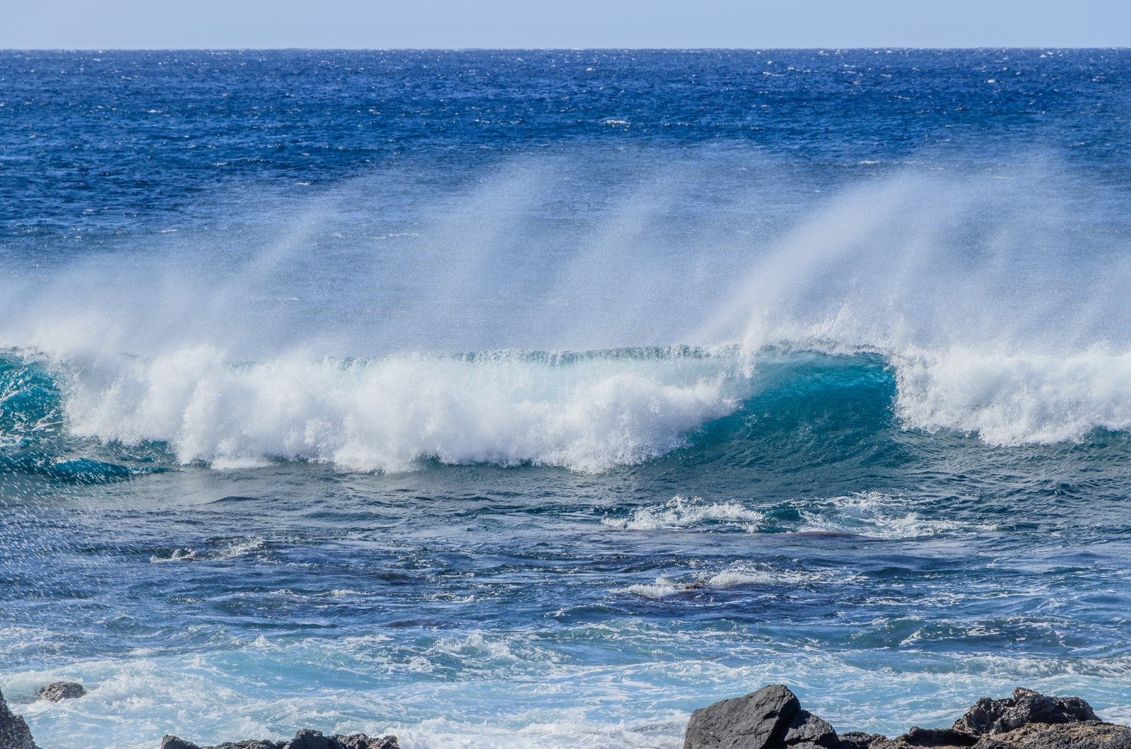 A powerful turquoise wave breaks with windblown spray in Valle Gran Rey.