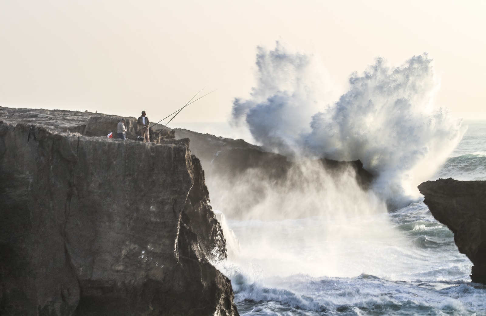 A powerful wave crashes against dark, rugged cliffs, sending white spray high into the air.