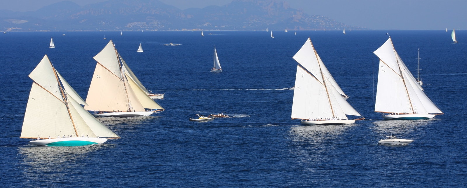 Classic sailing yachts with white sails billow in the wind during the Les Voiles de Saint-Tropez regatta.