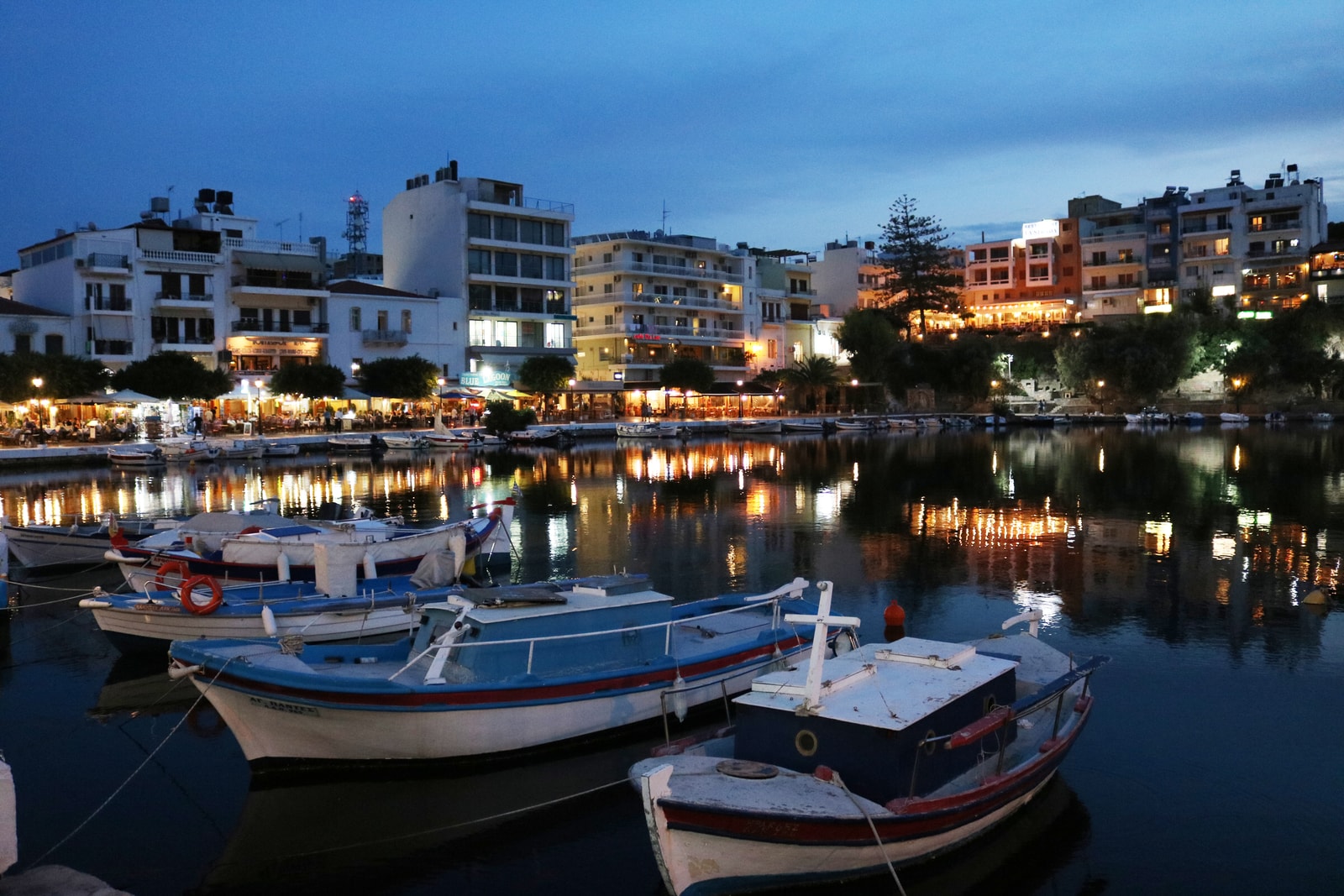 Boats moored in Voulismeni Lake at dusk, with waterfront lights reflecting on the calm water.