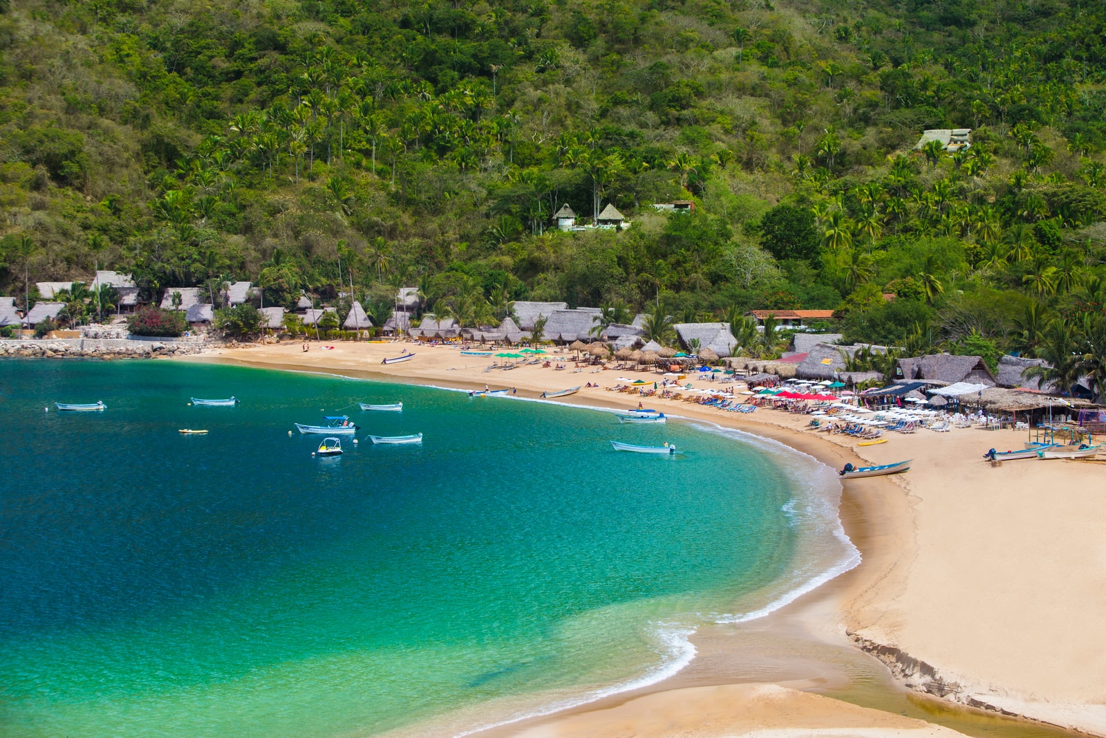 A wide, golden-sand beach curves around a tranquil bay, with the small village of Yelapa nestled in the lush jungle hillside.