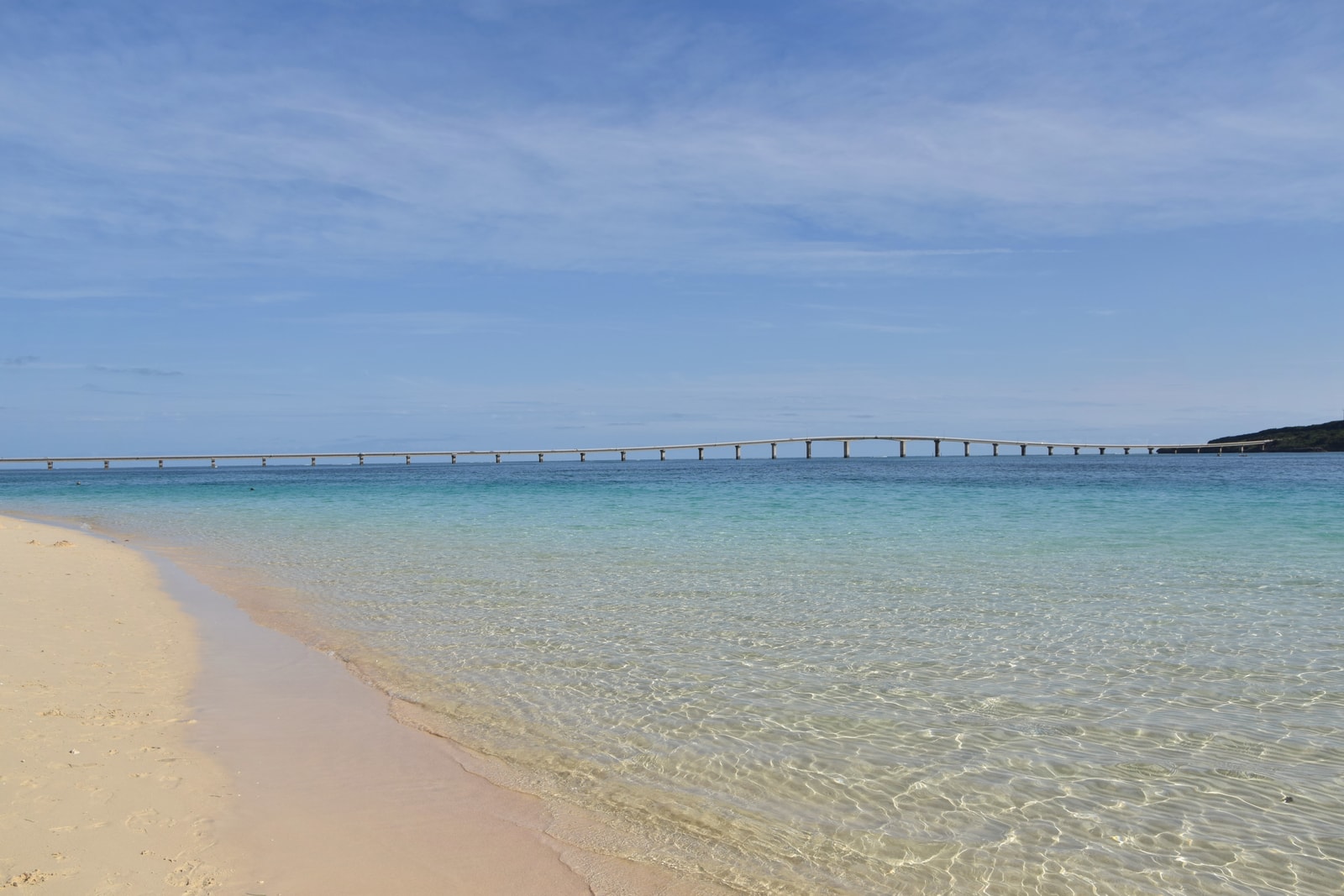 A vast expanse of white sand meeting calm, turquoise water under a clear blue sky.