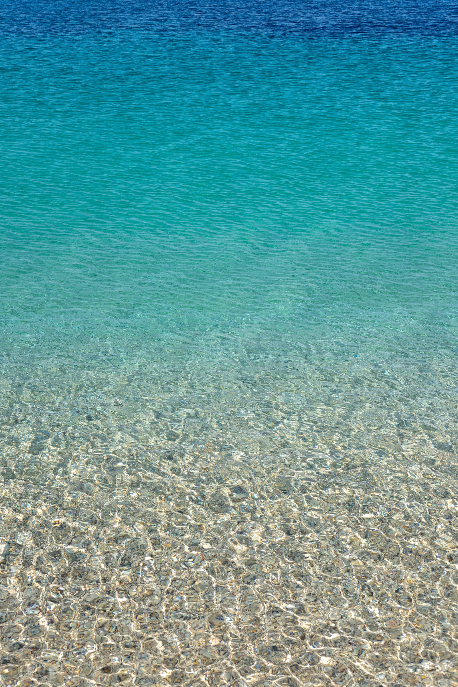 Sunlight filters through the crystal-clear water, illuminating the smooth white pebbles on the seabed.
