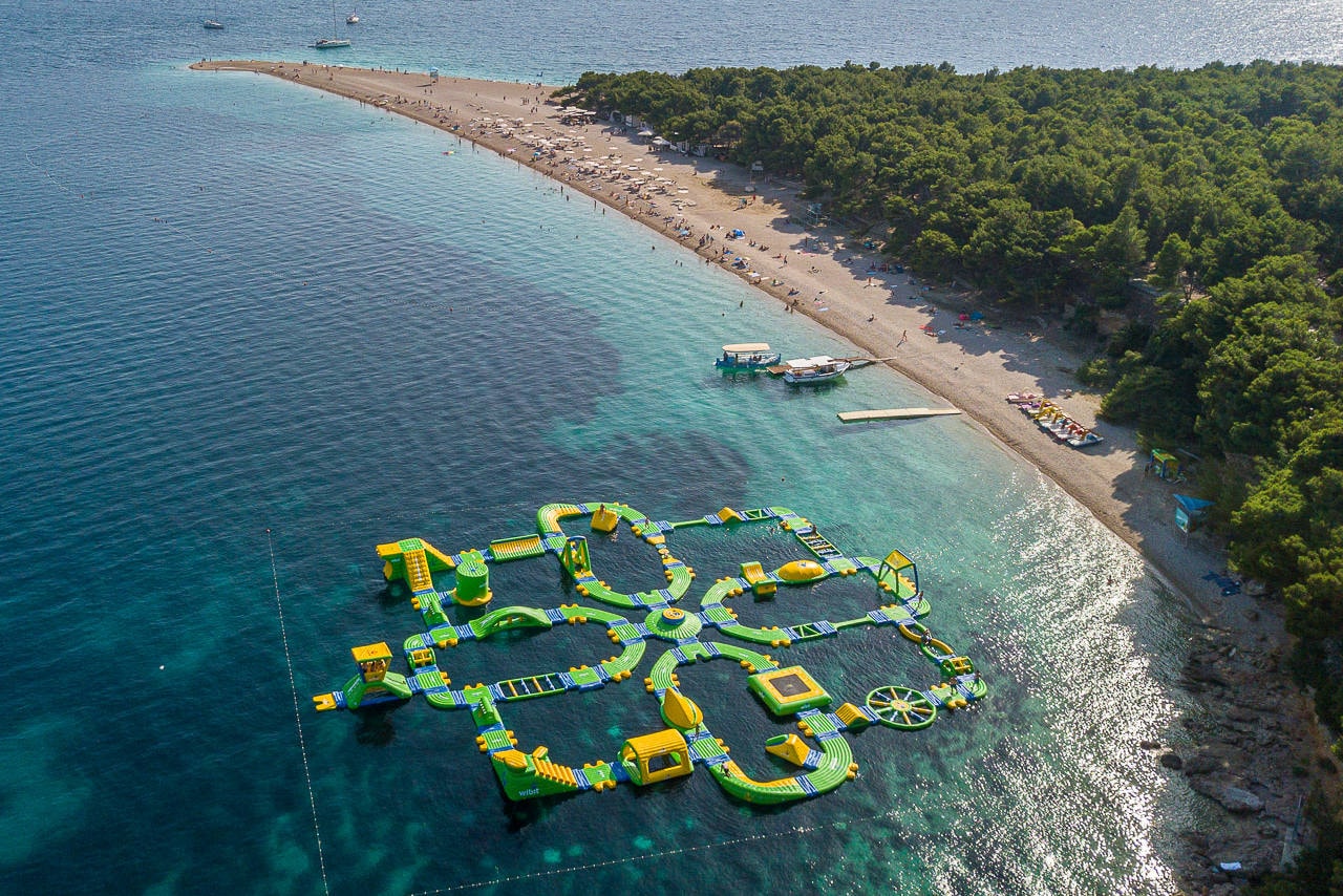 An inflatable aquapark with slides and climbing walls floats in the shallow water just off the beach.