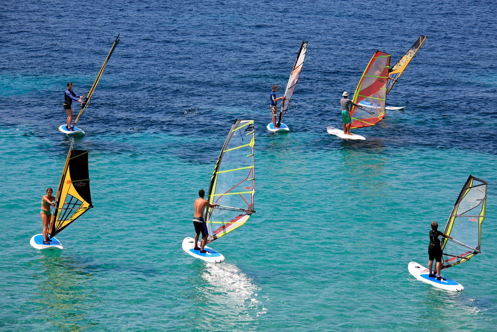 Several windsurfers glide across the turquoise waters off Zlatni Rat beach on a sunny day.