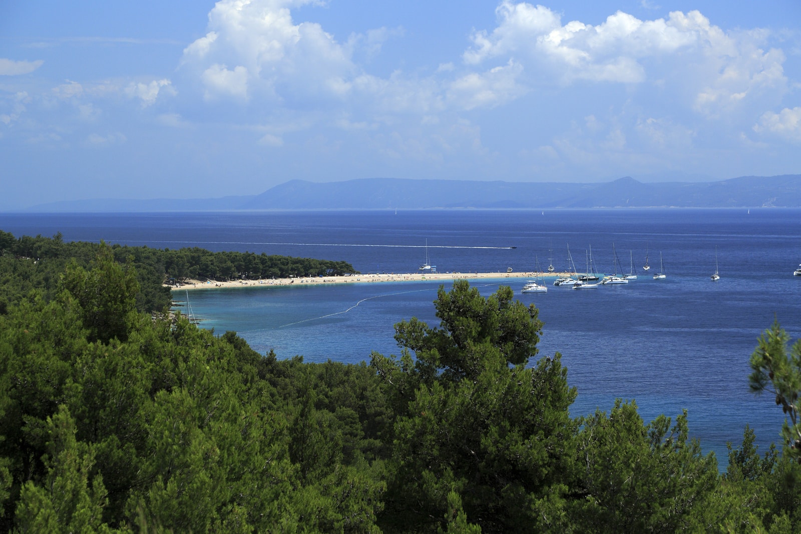 A view from a coastal road shows the Zlatni Rat spit jutting out from the rugged coastline of Brač.