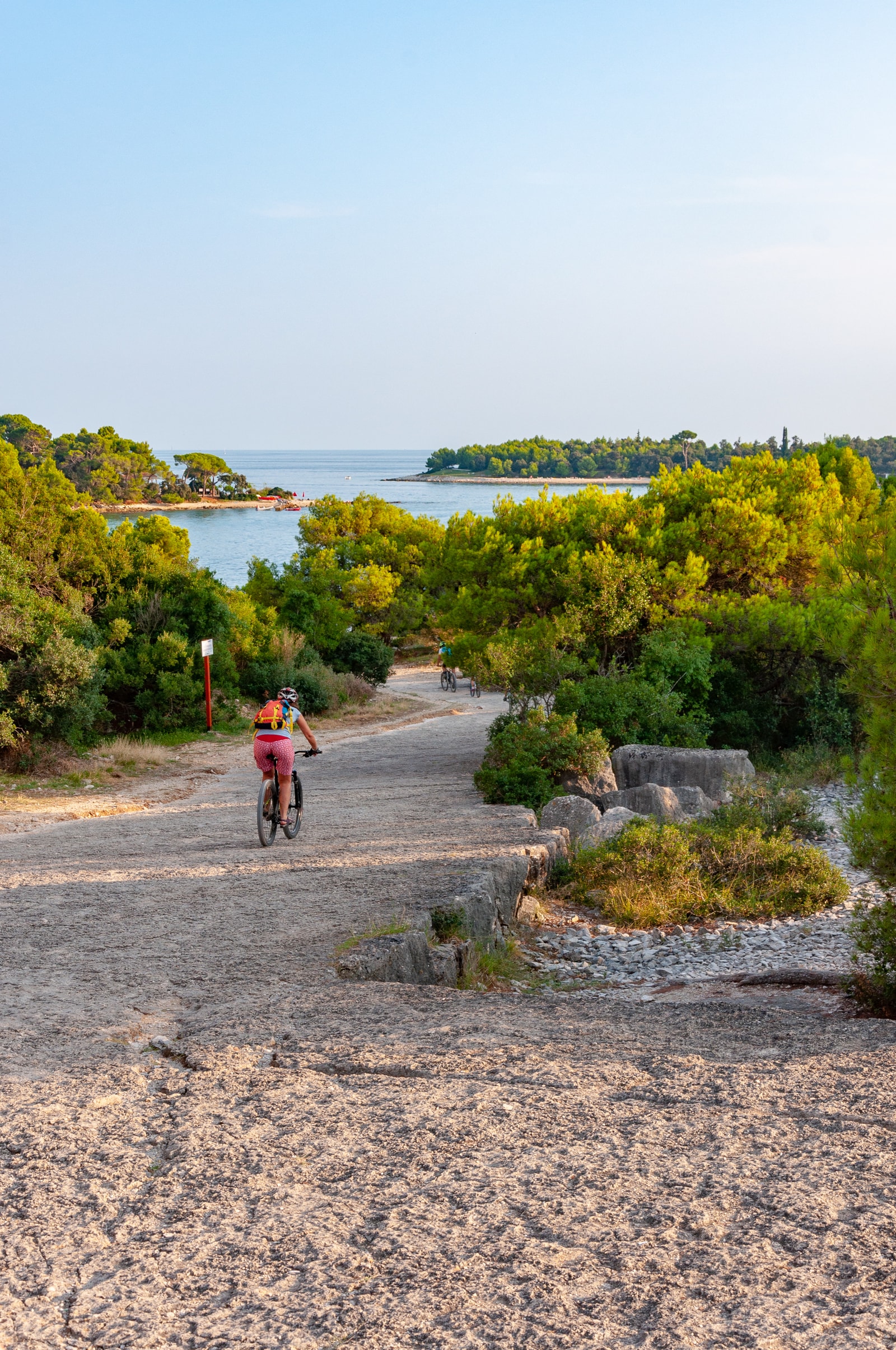 A cyclist rides along a coastal dirt path in the car-free Zlatni Rt forest reserve, with the sea visible in the background.
